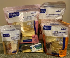 Several bags of Virbac C.E.T. enzymatic oral hygiene chews, recommended by veterinarians for dogs in various colors and sizes, are displayed on a carpeted floor.