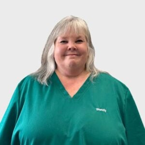 A veterinarian named Wendy, in a green scrub top with her name embroidered on it, smiling against a plain white background.