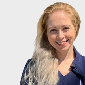 A smiling woman with long blonde hair wearing a navy blue veterinarian shirt, set against a plain white background.