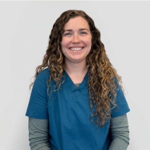 A veterinarian wearing a blue scrub top and smiling gently against a plain white background.